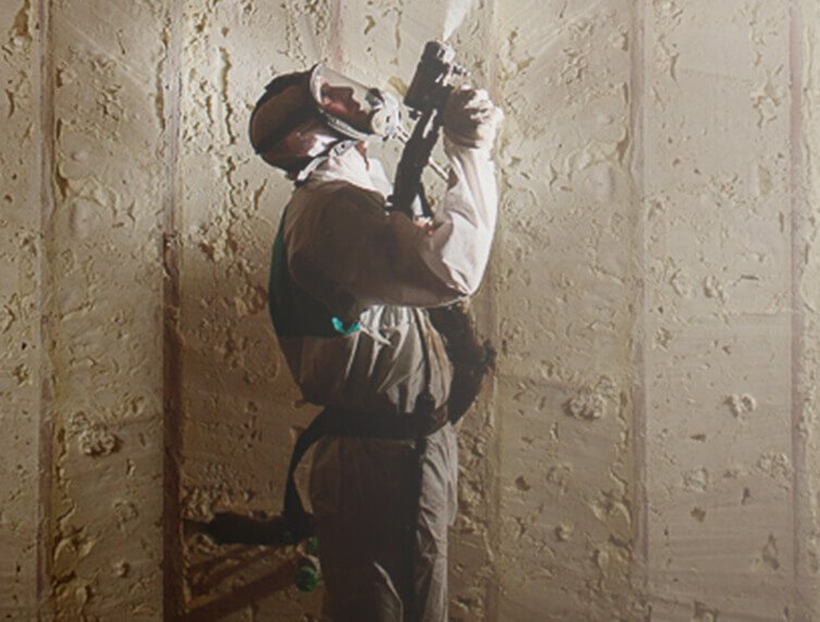Technician applying closed-cell spray foam insulation to a residential wall cavity